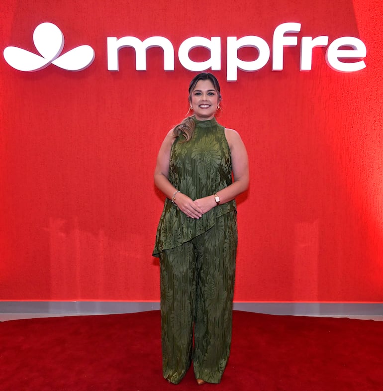 Mujer sonriente en conjunto verde floral, frente a fondo rojo con el logo de Mapfre iluminado.