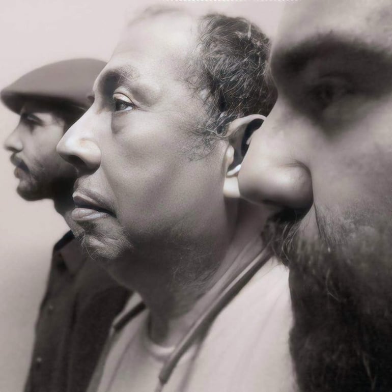 Tres hombres en perfil; el primero con boina y expresión seria, el segundo reflexivo y el tercero robusto y con barba desaliñada.