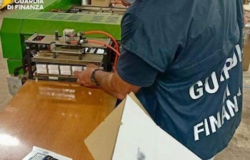 Oficial de la Guardia di Finanza en chaleco inspecciona equipo industrial mientras manipula objetos en un entorno de seguridad.