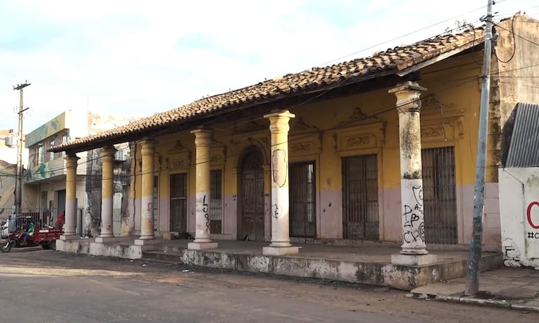 Estructura arquitectónica colonial deteriorada en un entorno urbano, con columnas blancas y amarillas, sin personas presentes.