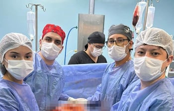 Cinco personas en quirófano, incluyendo un hombre con gorro rojo y tres hombres con gorros grises y negro, sosteniendo órgano extraído.