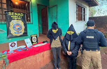 Tres personas en un entorno exterior; dos con capuchas y un agente de SENAD con vestimenta táctica, rodeados de evidencia en mesa.