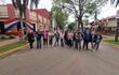 Grupo de personas en la calle, algunos con chaquetas y gorras, frente a un edificio gubernamental adornado con la bandera paraguaya.