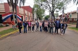 Grupo de personas en la calle, algunos con chaquetas y gorras, frente a un edificio gubernamental adornado con la bandera paraguaya.