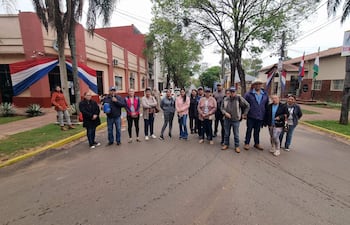 Grupo de personas en la calle, algunos con chaquetas y gorras, frente a un edificio gubernamental adornado con la bandera paraguaya.