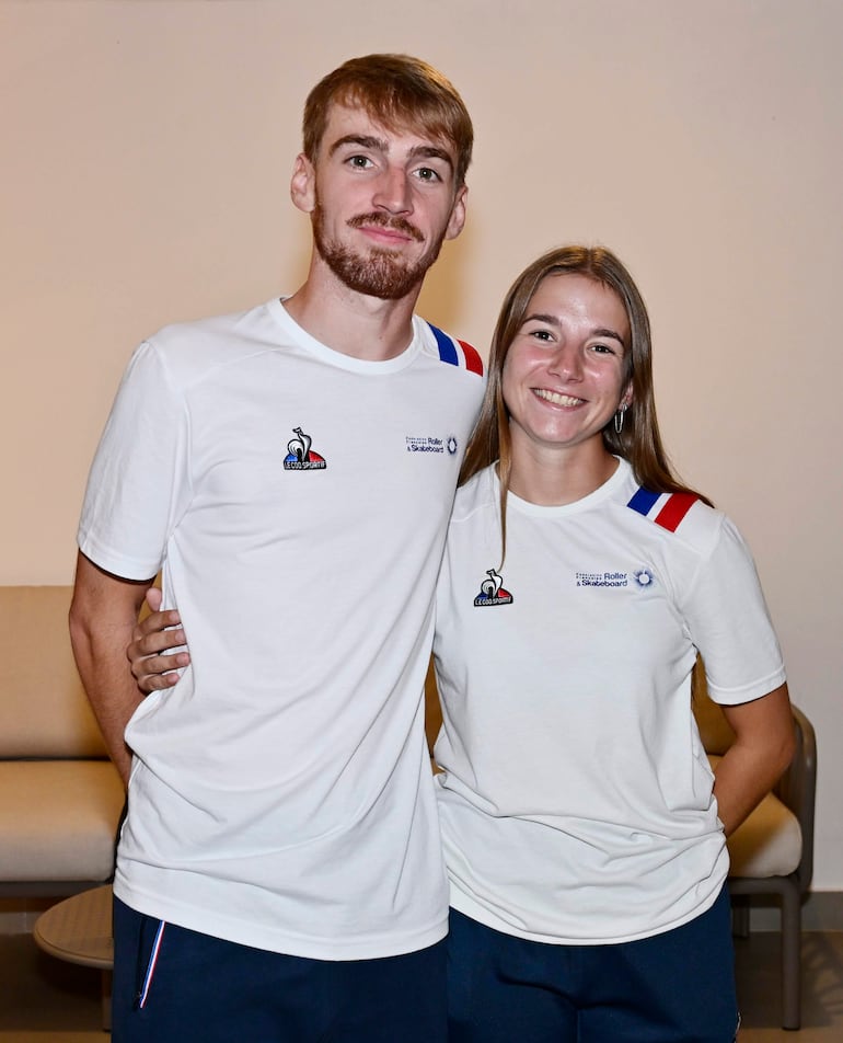 Pareja sonriente en coctel, el hombre con cabello rubio y barba, la mujer con cabello castaño, ambos en camisetas blancas con detalles en rojo y azul.
