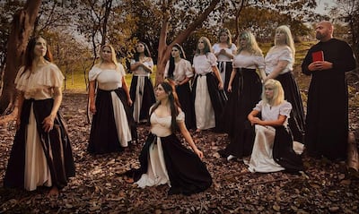 Grupo de 13 mujeres con faldas largas blancas y negras, organizadas en posiciones variadas junto a un hombre que sostiene un libro.