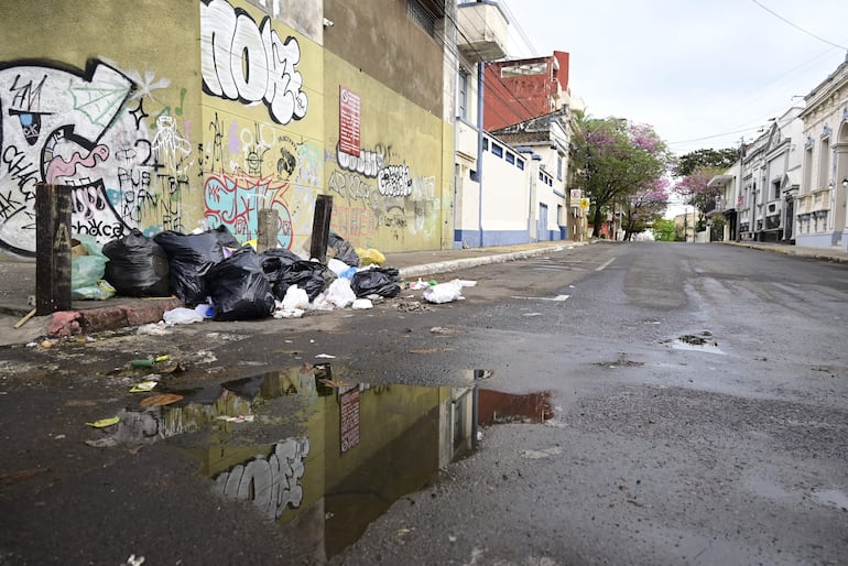 Calle desierta con bolsas de basura en la acera, rodeada de graffitis coloridos y pavimento húmedo.