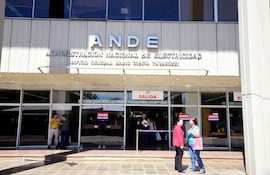 Tres hombres y dos mujeres conversan frente al edificio de la ANDE, bajo luz natural. Uno lleva chaqueta roja y otro camiseta amarilla.