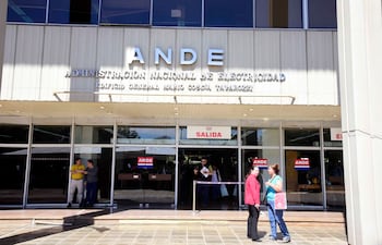 Tres hombres y dos mujeres conversan frente al edificio de la ANDE, bajo luz natural. Uno lleva chaqueta roja y otro camiseta amarilla.