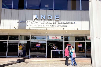 Tres hombres y dos mujeres conversan frente al edificio de la ANDE, bajo luz natural. Uno lleva chaqueta roja y otro camiseta amarilla.