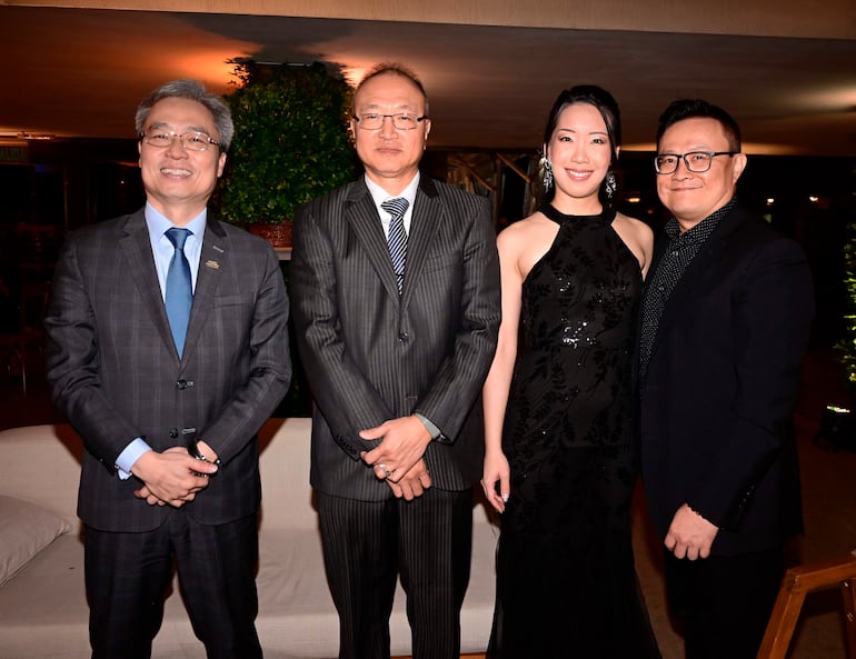 Iván Yueh-Jung Lee y Alida sonríen en un evento, luciendo trajes elegantes en un ambiente formal con luz suave.