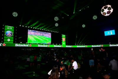 Ambiente oscuro con iluminación verde, pantalla grande mostrando acción del fútbol. No hay personas visibles.