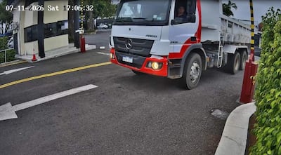 Camión Mercedes-Benz Atego avanza hacia entrada de Cóndor SACI, con barreras de seguridad y cielo nublado.