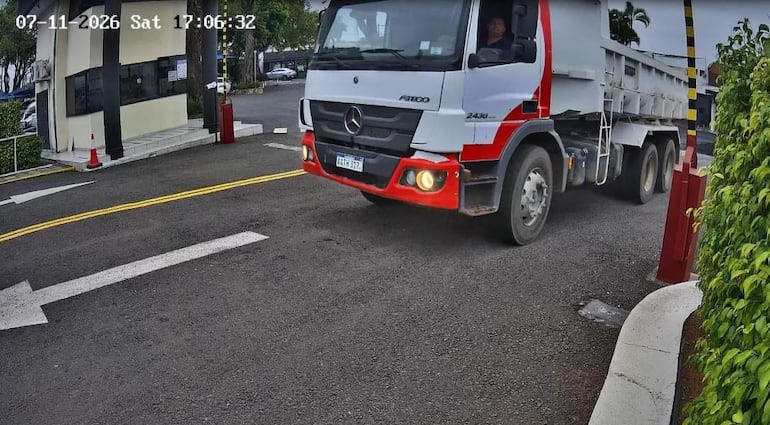 Camión Mercedes-Benz Atego avanza hacia entrada de Cóndor SACI, con barreras de seguridad y cielo nublado.