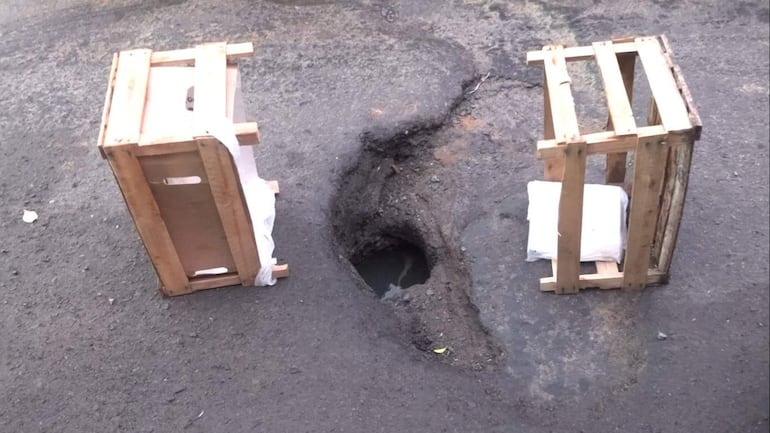 Agujero en pavimento urbano con cajas de madera a los lados, sin personas visibles ni elementos destacados.
