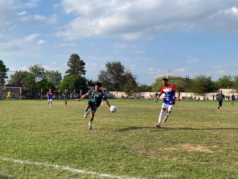 Jugadores con camisetas oscuras y de colores brillantes en campo de hierba, persiguiendo un balón bajo un ambiente de competencia deportiva.
