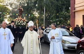 Monseñor Osmar López y dos sacerdotes en procesión religiosa, acompañados por jóvenes con la imagen de un santo entre decoraciones.