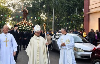 Monseñor Osmar López y dos sacerdotes en procesión religiosa, acompañados por jóvenes con la imagen de un santo entre decoraciones.