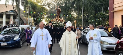 Monseñor Osmar López y dos sacerdotes en procesión religiosa, acompañados por jóvenes con la imagen de un santo entre decoraciones.