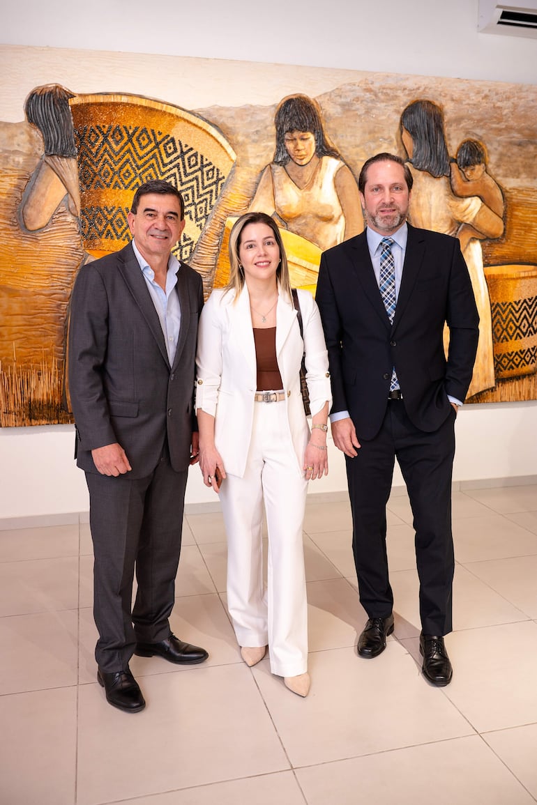 Jorge Moreno sonriente en traje oscuro, Claudia Vallejos con traje blanco y Paul Sarubbi en traje oscuro, frente a un mural cultural.