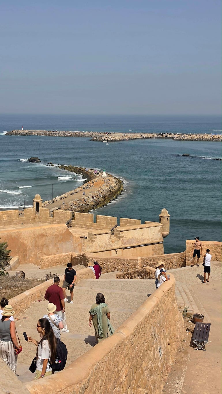 Mujer con sombrero claro y otra persona sostenido un móvil, disfrutando del clima cálido en la costa.