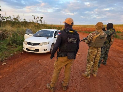 Agentes de la SENAD en chalecos tácticos y gorras, observan cuidadosamente un vehículo blanco en un entorno rural.