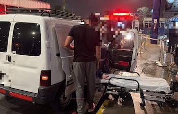 Hombre en uniforme coordina el traslado de un paciente en camilla hacia un furgón blanco en la noche.