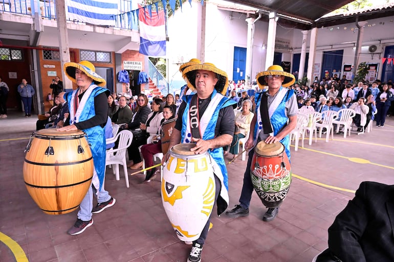 Viviana Stella Duarte Bojanovich entre el público durante la celebración, mientras hombres con sombreros amarillos tocan tambores.