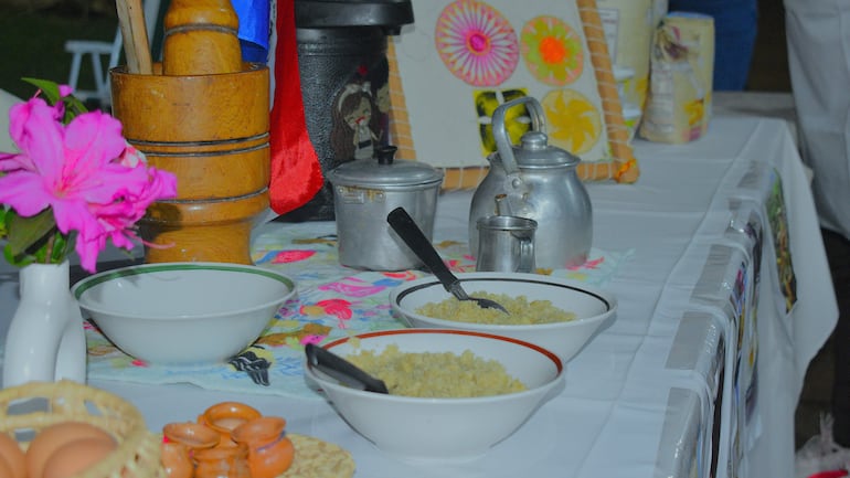 Mesa con platos típicos, utensilios de cocina y decoración floral, en ambiente festivo sin personas visibles.