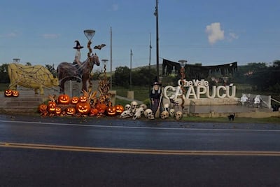 Escultura de caballo amarillo y marrón con telarañas, bruja con escoba y calabazas en un ambiente festivo de Halloween.