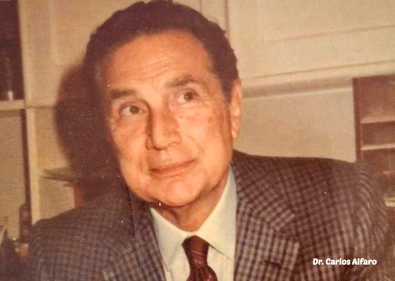 INDEGA. Dr. Carlos Alfaro en retrato formal, vistiendo traje y corbata, con fondo neutro.