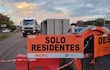 Cartel de 'SOLO RESIDENTES' en construcción vial, con casas y un camión en el fondo bajo un cielo nublado.