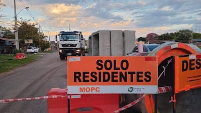 Cartel de 'SOLO RESIDENTES' en construcción vial, con casas y un camión en el fondo bajo un cielo nublado.