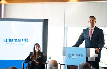 Peña en traje oscuro y corbata roja, habla en un podio ante un público no visible en un ambiente iluminado por un gran ventanal.
