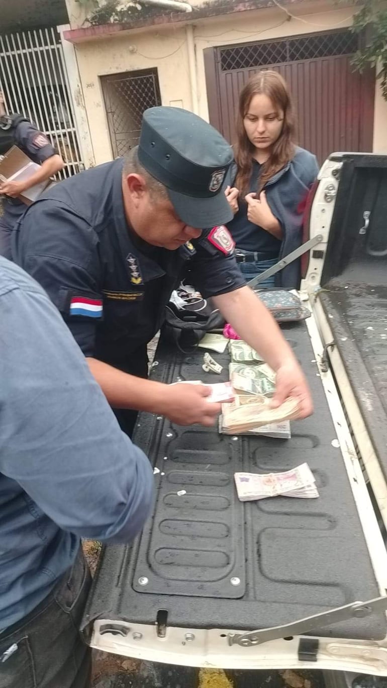 Agente policial en uniforme y gorra cuenta billetes en una superficie, mientras una mujer lo observa atentamente en un ambiente urbano.
