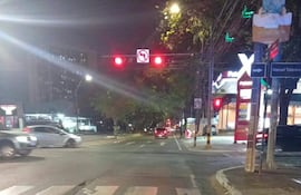 Motociclista en su vehículo parado, con semáforo en rojo y entorno urbano iluminado por farolas y negocios.