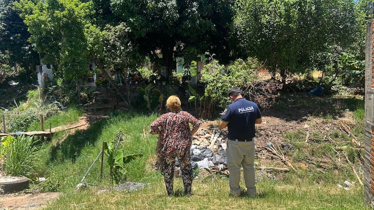 Natividad González, vecina del barrio San Carlos de Ñemby, nuestra a un agente policial del DEBOA el desastre ambiental causado por la acumulación de basura en el curso de agua.