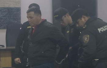 Roberto Cubilla Sanabria con chaqueta negra mientras un policía le quita las esposas, rodeado de agentes uniformados en un ambiente de detención.