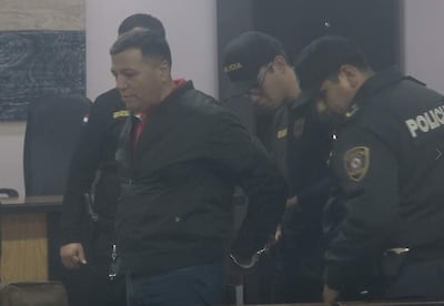 Roberto Cubilla Sanabria con chaqueta negra mientras un policía le quita las esposas, rodeado de agentes uniformados en un ambiente de detención.