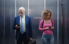Hombre y mujer miran su celular en un ascensor.