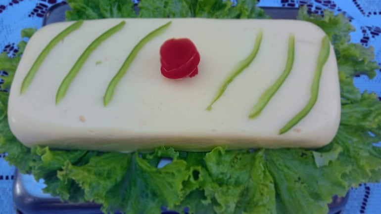 Plato decorado con gelatina sobre lechuga, aderezado con tiras verdes y una rosa roja, en mesa al aire libre.