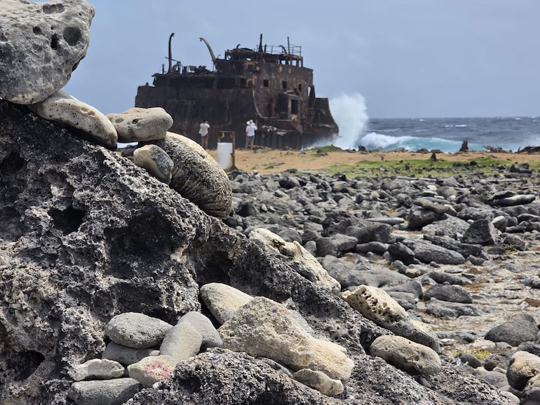 Faro gris con detalles rojos rodeado de un paisaje árido y cielo nublado, sin personas visibles.
