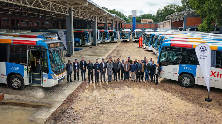 Grupo de personas en trajes formales y casuales, posando frente a autobuses Volkswagen en un entorno profesional al aire libre.