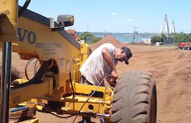 Un operario en tareas de mantenimiento a una máquina vial de la Gobernación. Al fondo el majestuoso puente internacional "San Roque González de Santa Cruz", que une con Posadas, Argentina.