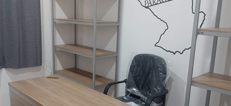 Espacio interior vacío con mobiliario nuevo de madera y metal, estanterías y un mapa de Paraguay en la pared.