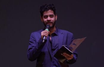 Hombre en traje oscuro, con micrófono y documento en mano, hablando en un escenario oscuro durante los Premios Edda.