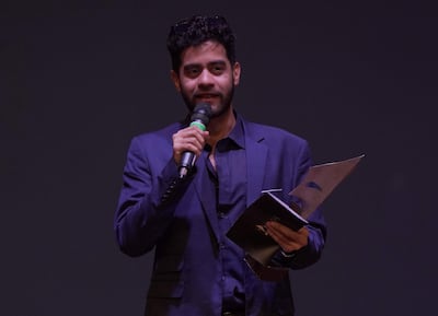 Hombre en traje oscuro, con micrófono y documento en mano, hablando en un escenario oscuro durante los Premios Edda.
