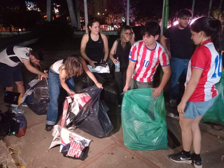 Seis personas, entre ellas un hombre de camiseta blanca y una mujer con camiseta de la selección paraguaya, recogen basura en un entorno urbano.