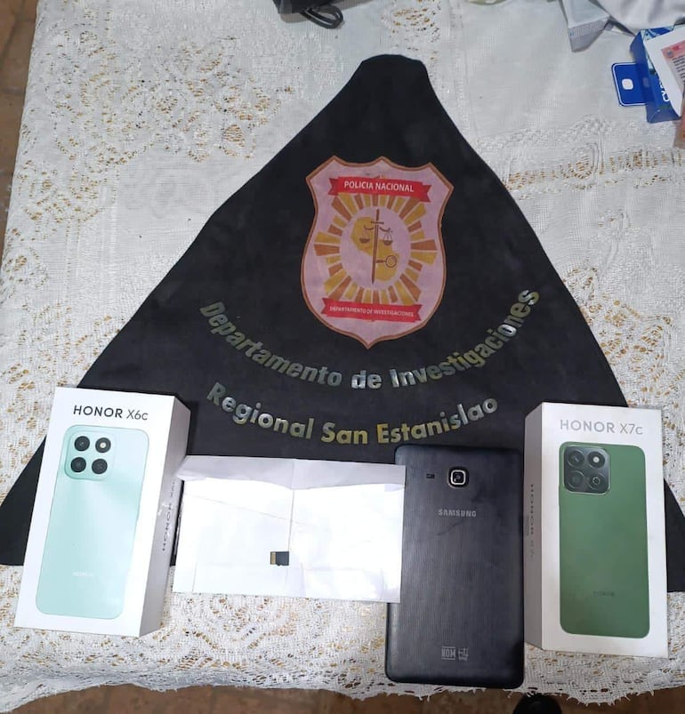 Mesa con el emblema de la Policía Nacional, cajas de teléfonos Honor y un Samsung, en un ambiente policial cerrado.
